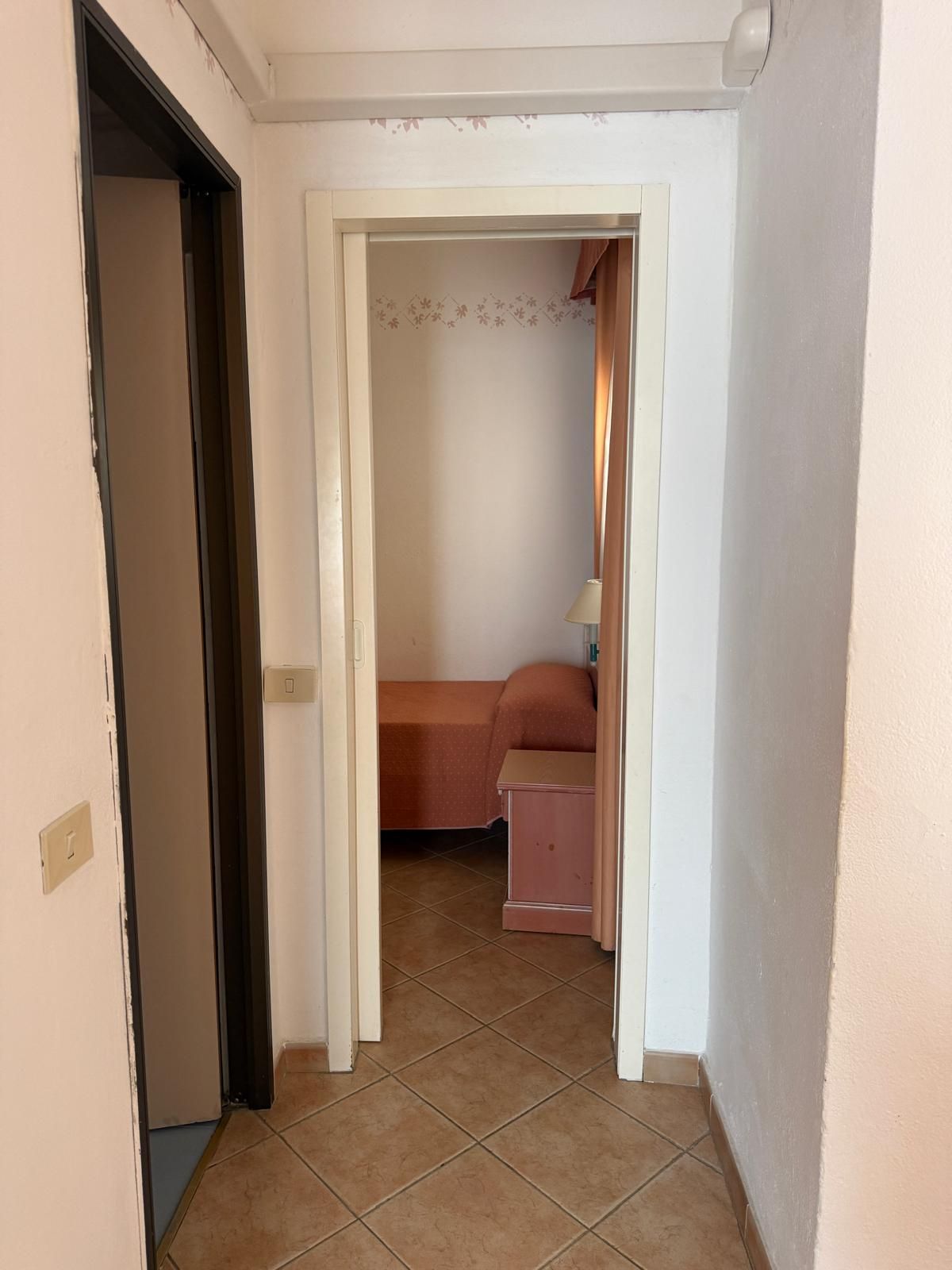 Un corridoio stretto che porta a una camera da letto con un letto e un comodino.