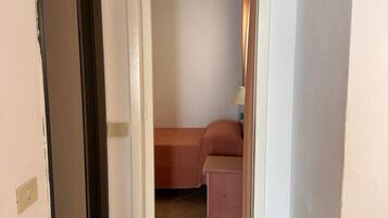 Een smalle gang die uitkomt in een slaapkamer met een bed en nachtkastje.
