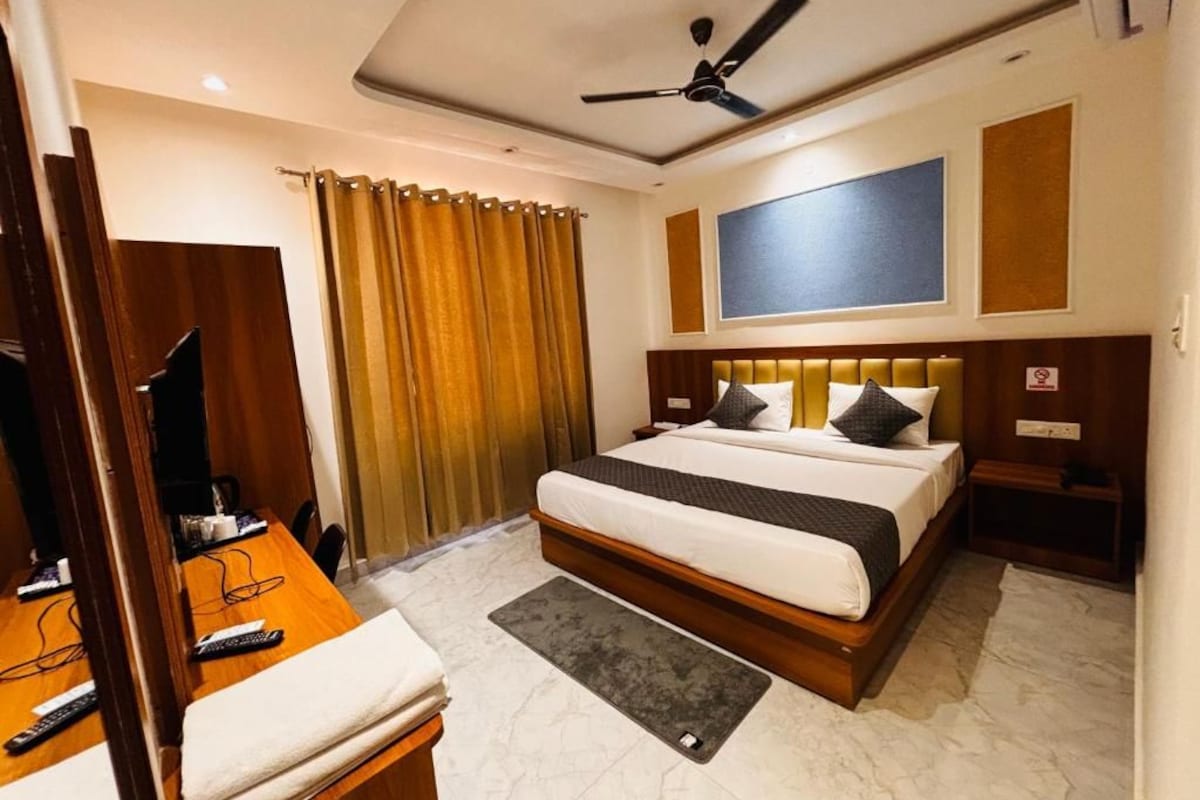 A hotel room with a bed, a desk with a chair, a ceiling fan, and a window with curtains.