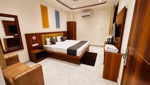 A hotel room with a bed, a seating area, a ceiling fan, an air conditioning unit, and a wooden wardrobe. - Hotel Shivay Palace (Rishikesh)