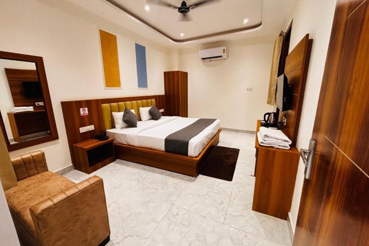 A hotel room with a bed, a seating area, a ceiling fan, an air conditioning unit, and a wooden wardrobe.