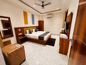 A hotel room with a bed, a seating area, a ceiling fan, an air conditioning unit, and a wooden wardrobe. - Hotel Shivay Palace (Rishikesh)