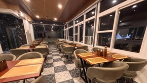 A restaurant interior with hexagonal patterned flooring, tables with chairs, and large windows. - Hotel Shivay Palace (Rishikesh)