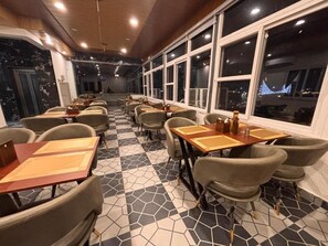 A restaurant interior with hexagonal patterned flooring, tables with chairs, and large windows. - Hotel Shivay Palace (Rishikesh)