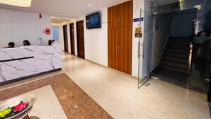 A hotel reception area with a marble counter, wooden doors, a glass elevator, and a staircase. - Hotel Shivay Palace (Rishikesh)