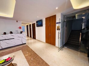 A hotel reception area with a marble counter, wooden doors, a glass elevator, and a staircase. - Hotel Shivay Palace (Rishikesh)