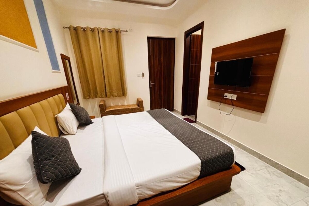 A hotel room with a bed, a television mounted on the wall, and a window with curtains.