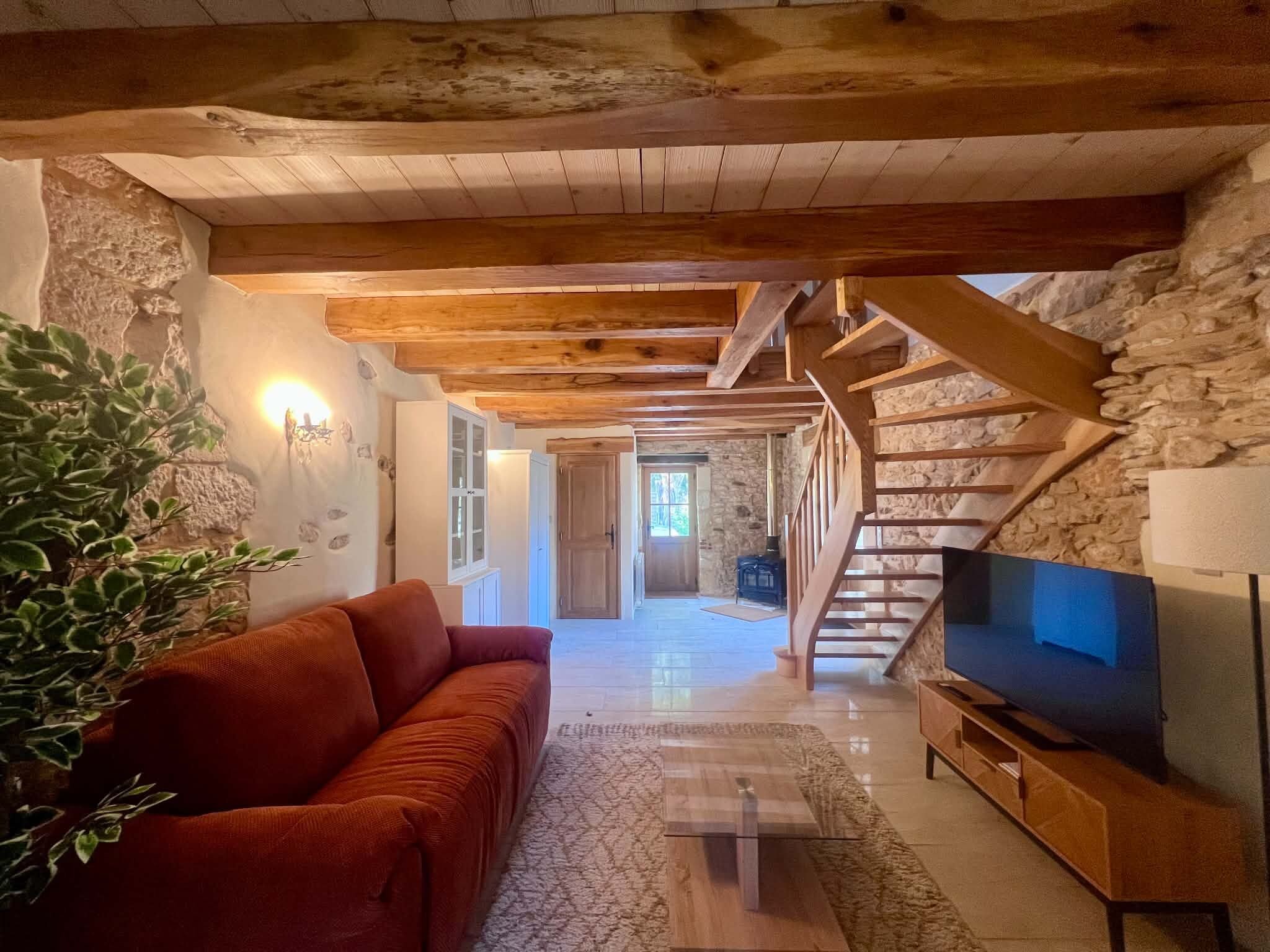 A cozy living room with a wooden staircase, a red sofa, and a TV.