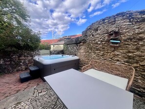 Ein Whirlpool mit Steinwand im Hintergrund, einem Tisch und einem Korbstuhl.