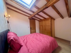 Ein Schlafzimmer mit Oberlicht, Holzbalken, einem Bett mit rosa Bettwäsche und einem Nachttisch.
