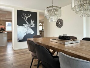 A dining area with a wooden table, chairs, a chandelier, and a wall-mounted artwork of a deer. - Romantic Chalet Neuastenberg (Winterberg)