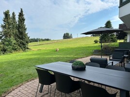 Un patio exterior con una mesa y sillas, césped y árboles al fondo.