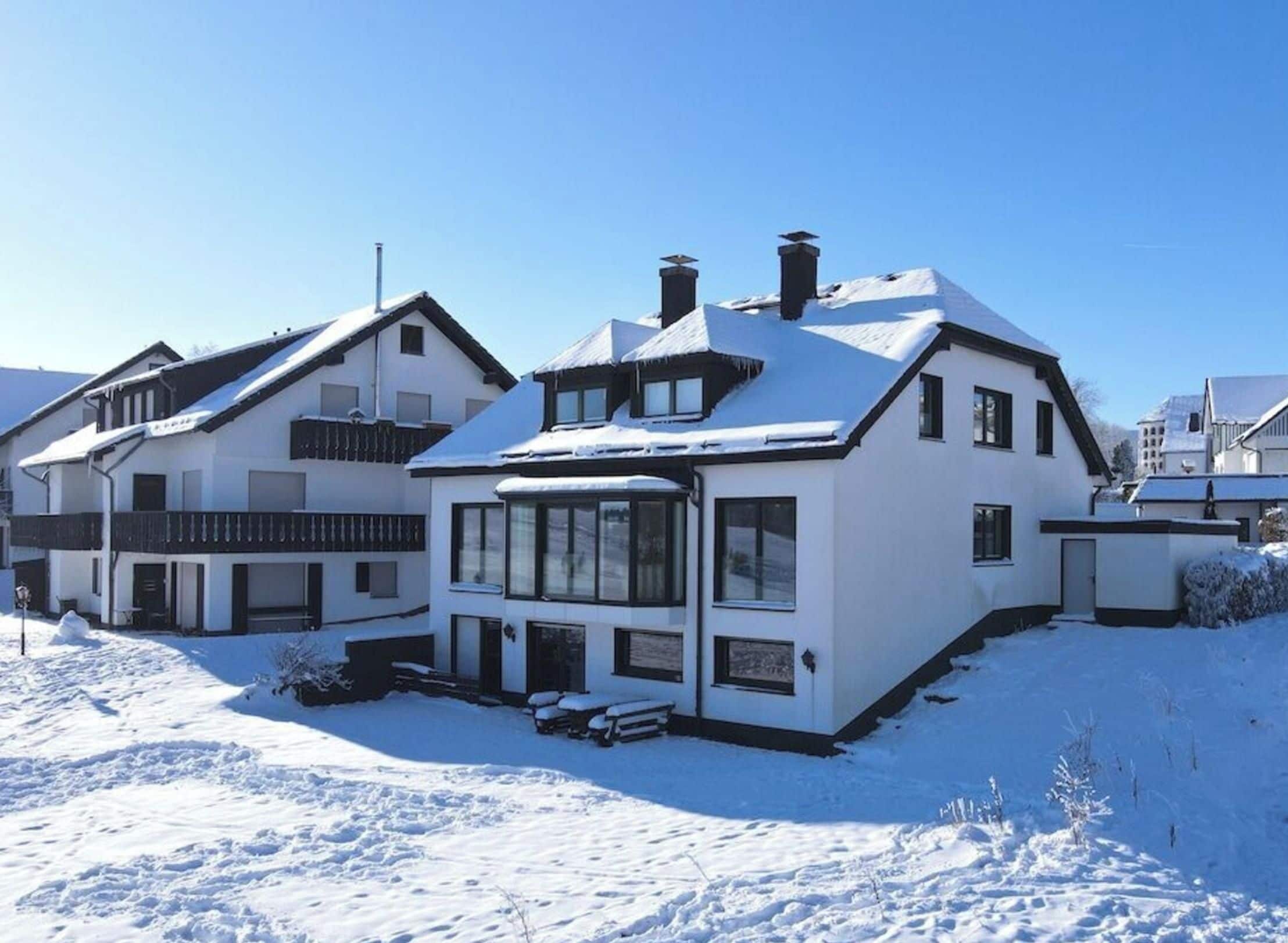 A two-story house with a snow-covered roof and a large window on the ground floor.