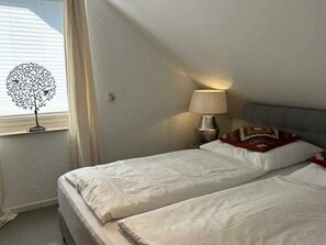A bedroom with two beds, a lamp, a decorative tree, and a window with blinds. - Romantic Chalet Neuastenberg (Winterberg)