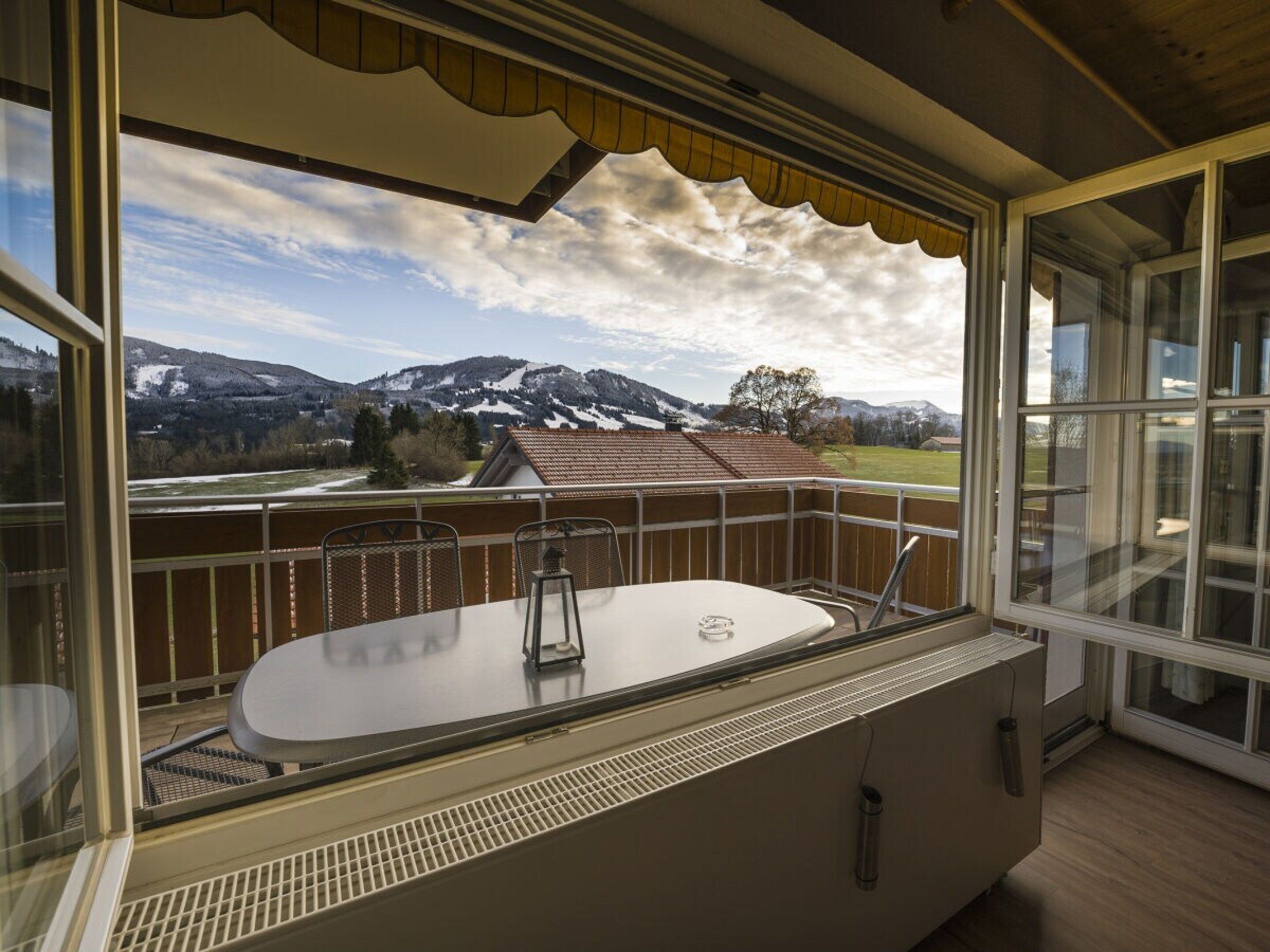 Ein Balkon mit Tisch und Stühlen, Blick auf schneebedeckte Berge und Geländer aus Holz.