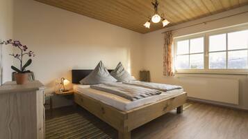 Ein Schlafzimmer mit einem hölzernen Bett, einem Nachttisch, einer Lampe, einem Fenster mit Vorhängen und einer Orchidee im Blumentopf.