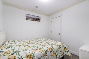 Ein Schlafzimmer mit einem Bett, einer Tür, einer weißen Wand und einem gerahmten Bild.
