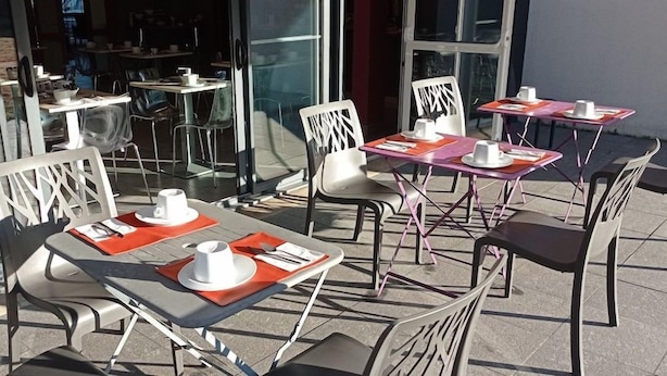 Un área de estar al aire libre con mesas y sillas, algunas con individuales anaranjados y servilletas blancas.