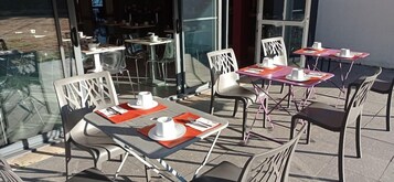 Un espace extérieur aménagé avec des tables et des chaises, dont certaines sont agrémentées de sets de table orange et de serviettes blanches.