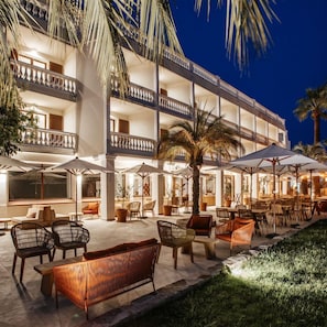 Un hotel de varios pisos con asientos exteriores y palmeras.