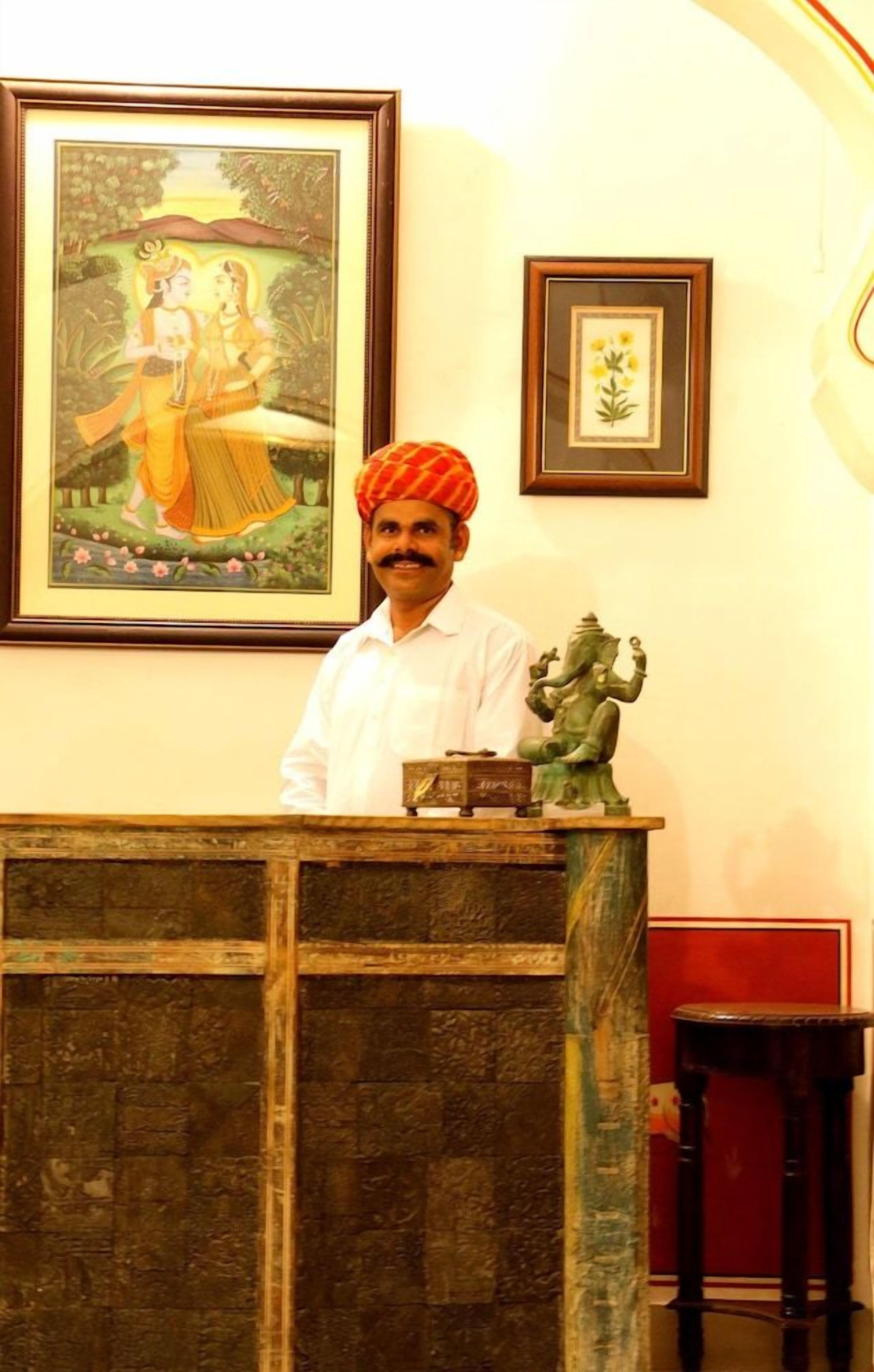 A man standing behind a reception desk with framed artwork and a statue on the wall.