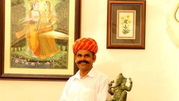 A man standing behind a reception desk with framed artwork and a statue on the wall.