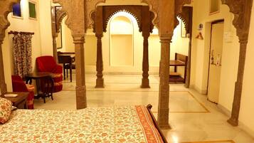 A room with a bed, a table, chairs, and a small desk. There are arches and columns in the architecture.
