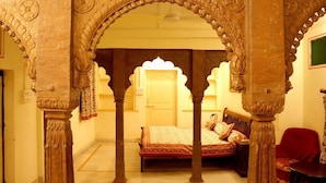 Una habitación con una cama, una silla roja y un pórtico ornamentado con detalles tallados.
