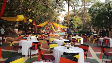 An outdoor event with round tables and chairs, decorated with drapes and flowers.