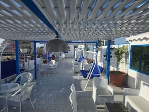 An outdoor seating area with white wicker furniture, a hanging chair, and a blue hammock. - Rahhal Al Bahr Hotel Apartment (Jeddah)