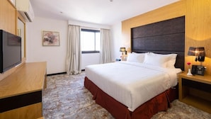 A hotel room with a bed, bedside lamps, a TV, and a window with curtains. - Mira Hotel (Riyadh)