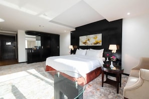 Una habitación de hotel moderna con una cama grande, una mesa de centro de cristal, una silla y un cuadro en la pared.