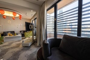 Una sala de estar moderna con un sofá, una mesa de centro y un televisor. Se ve un gran ventanal con vistas a edificios.