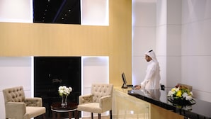 A modern hotel lobby with a reception desk, seating area, and a view of the sky through a large window. - Mira Hotel (Riyadh)