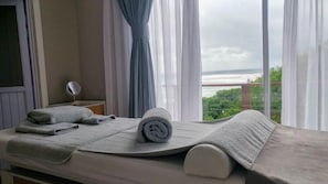 A room with a bed, a small table with a mirror, and a view of the sea.