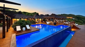 Ein Resort mit einem großen Schwimmbecken, Außenbereich zum Sitzen und mehreren Bungalows über dem Wasser.