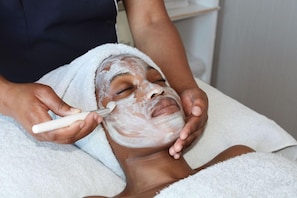 Uma pessoa recebendo tratamento facial, com uma toalha branca e um tecido branco na cabeça.