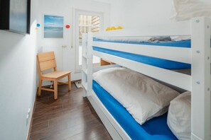 Quarto com beliche, uma cadeira de madeira, uma mesa pequena e uma porta que dá para o exterior.