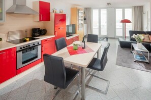 Una cocina moderna con armarios rojos, una zona de comedor con mesa y sillas, y una sala de estar con sofá y mesa de centro.