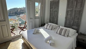A bedroom with a large bed, a view of the outdoors, and a balcony. - Niriides Apartaments (Symi)