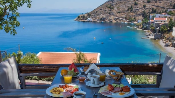 A table set with breakfast items and a scenic view of a coastal area. - Niriides Apartaments (Symi)