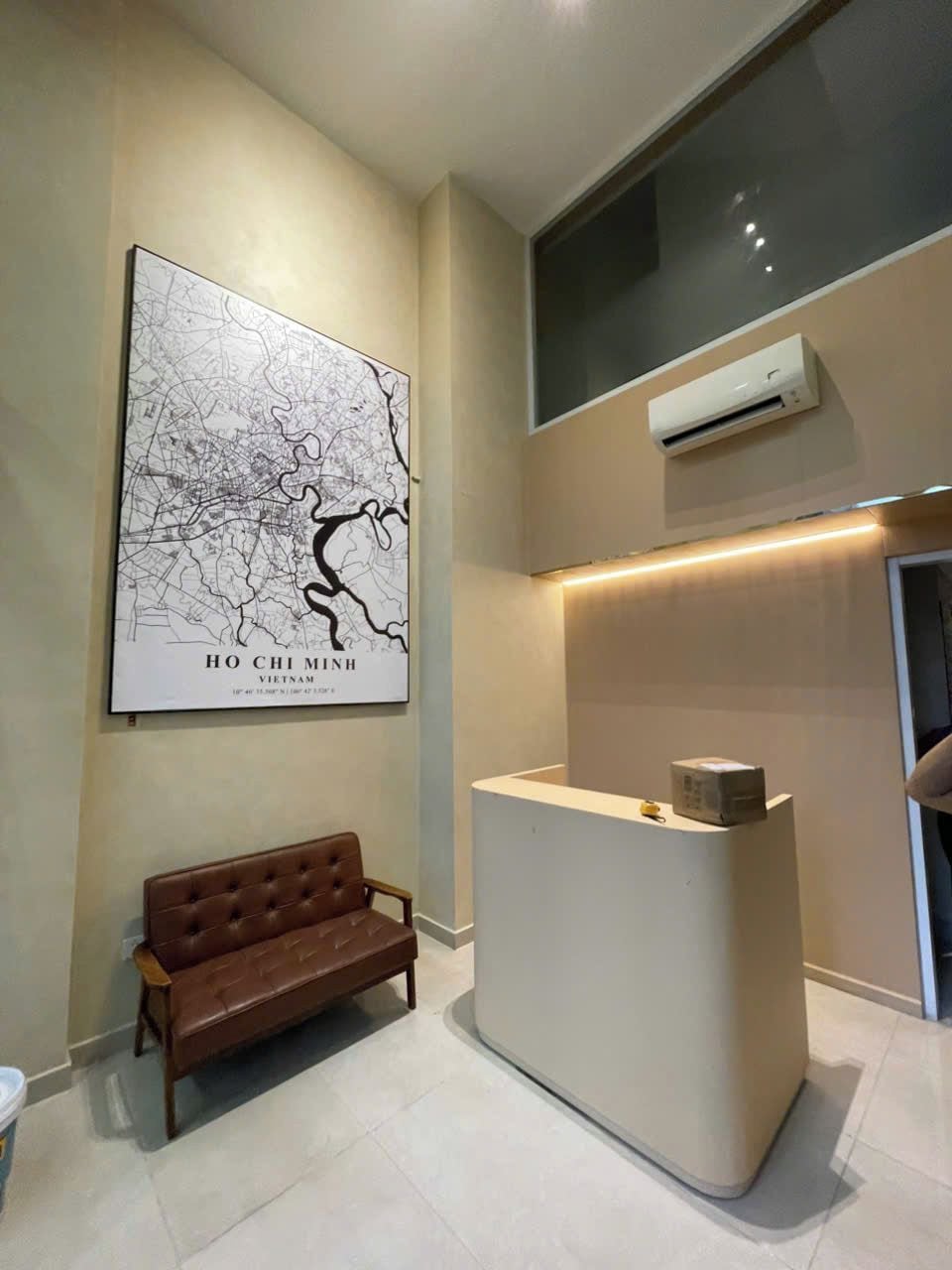 Un mostrador de recepción con un mapa de Ho Chi Minh, Vietnam, un banco de cuero marrón y una unidad de aire acondicionado.