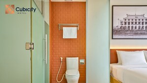 Un baño de hotel con inodoro, toallero y cama con ropa blanca.