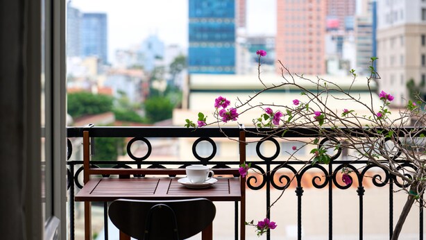 A balcony with a table and chair, overlooking a cityscape with buildings. - Cubicity Nguyen Truong To (Ho Chi Minh)