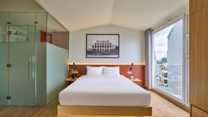 A modern hotel room with a large bed, a glass shower enclosure, a framed picture on the wall, and a city view through the window. - Cubicity Nguyen Truong To (Ho Chi Minh)