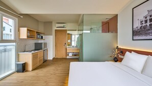 A modern hotel room with a kitchenette, a bed, and a bathroom with a glass partition. - Cubicity Nguyen Truong To (Ho Chi Minh)