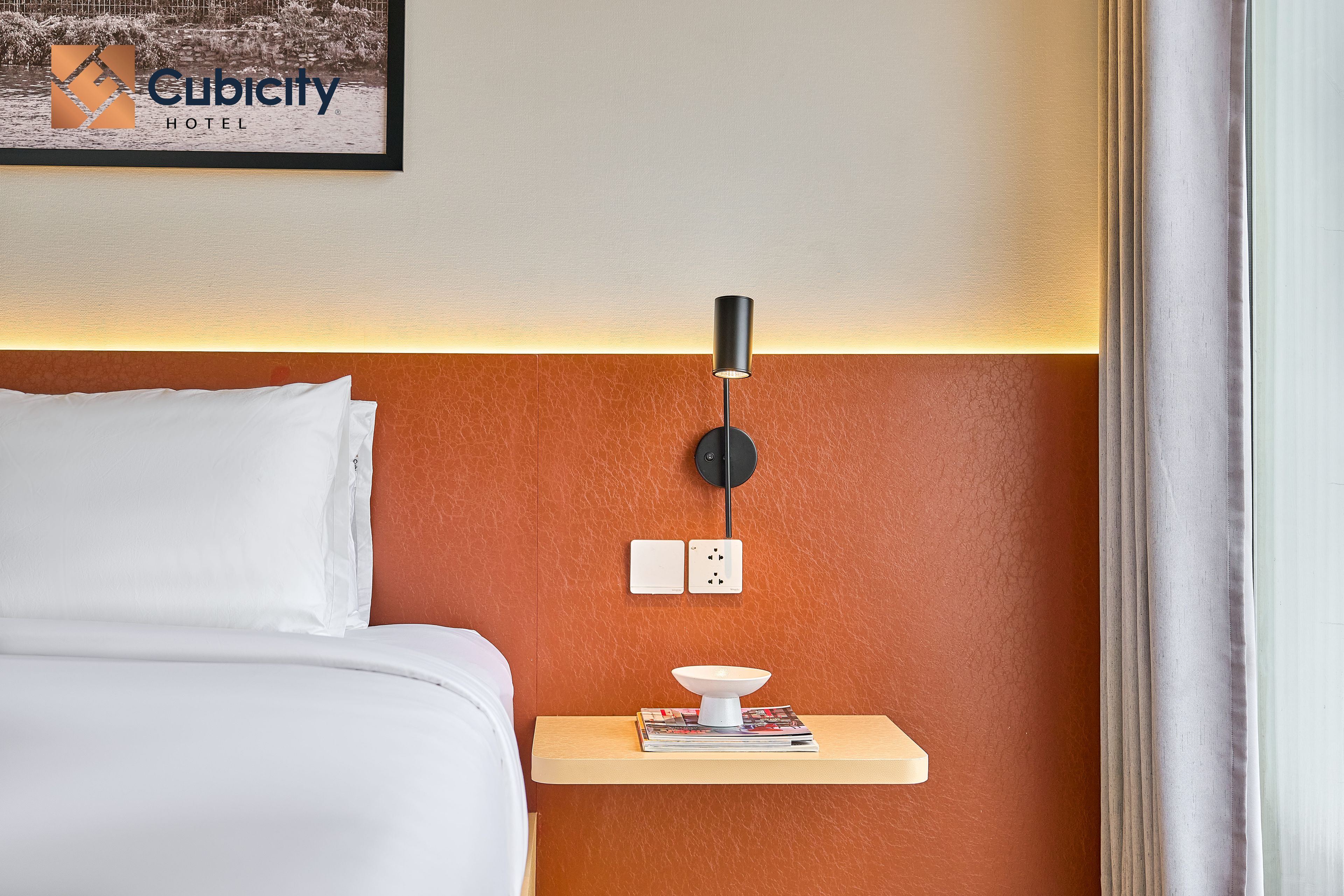 Une chambre d’hôtel avec un lit, une table de chevet avec une lampe et une prise de courant fixée au mur.