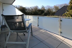 An outdoor balcony with a table and chairs, a white wall, and a solar panel in the background. - 6 at Gmelinstraße 23 (Wyk auf Föhr)