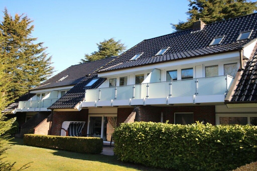 Une rangée de maisons de ville avec un toit en pente, un porche abrité et une haie bien entretenue à l’avant.