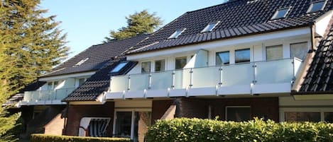 Une rangée de maisons de ville avec un toit en pente, un porche abrité et une haie bien entretenue à l’avant.